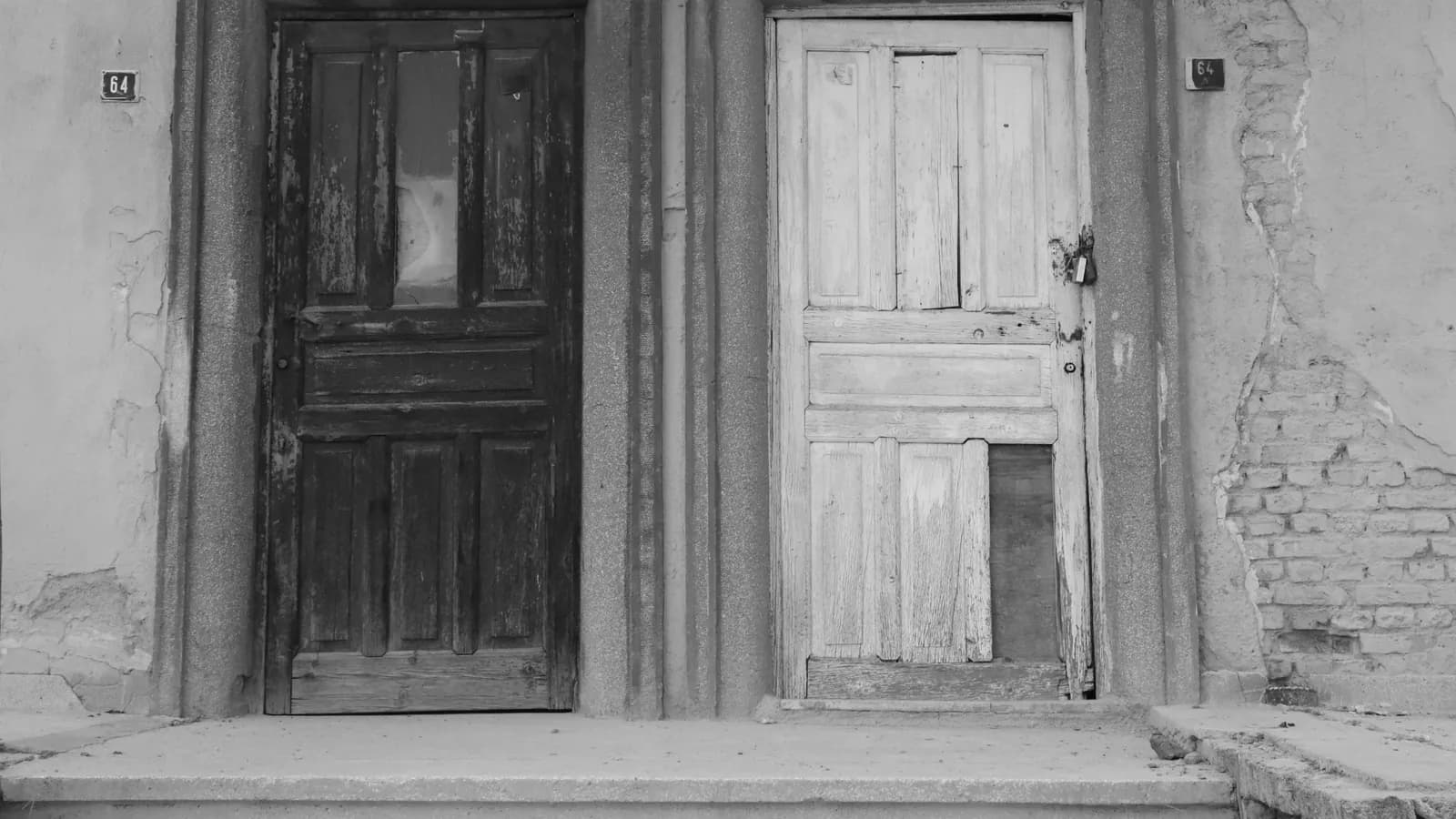 Köhnə binanın fasadında yan-yana yerləşən iki fərqli rəngli taxta qapı, ağ-qara fotoda, hər ikisinin üstündə 64 nömrəsi asılıb.