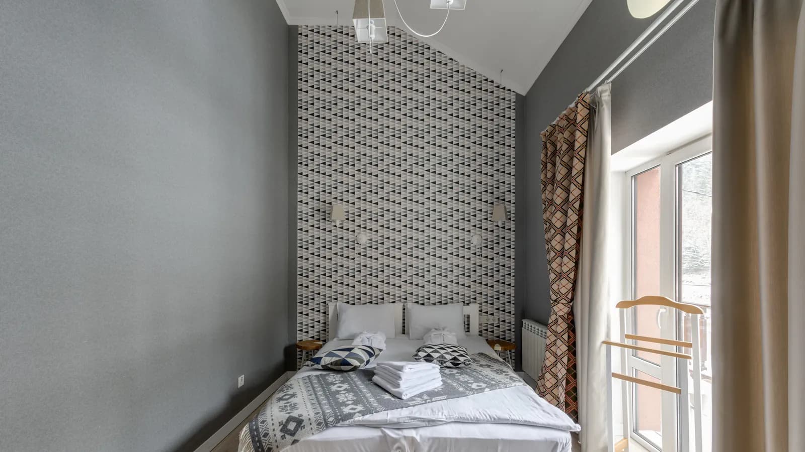 Günəş işığı pəncərədən düşən, səliqəli ağ yorğan-döşəklə örtülmüş otel otağının mənzərəsi.