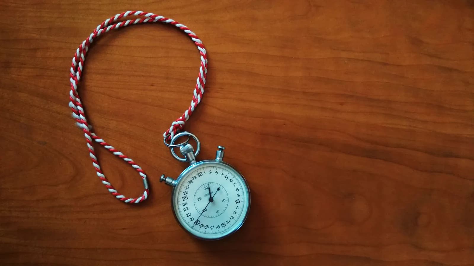 Taxta masanın üstündə mexaniki saniyəölçən: qırmızı-ağ burma bağı yanında halqa şəklində qoyulub, ağ siferblatda saniyələr 0-dan 30-a qədər nömrələnib.